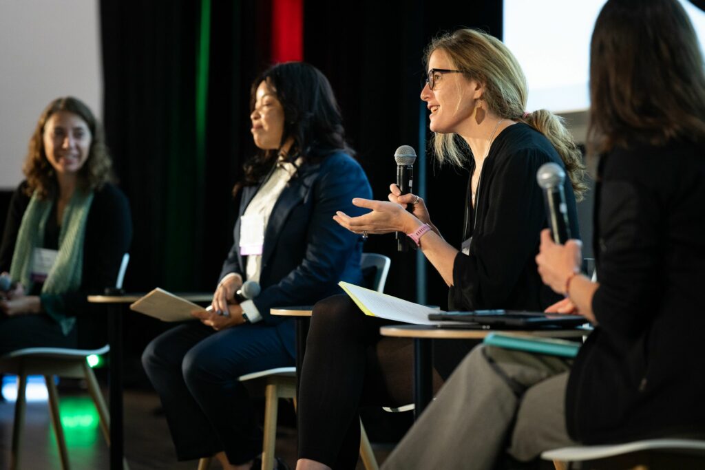 Lauren E. Oakes, scientist and author, is speaking into a microphone while others on stage listen attentively.